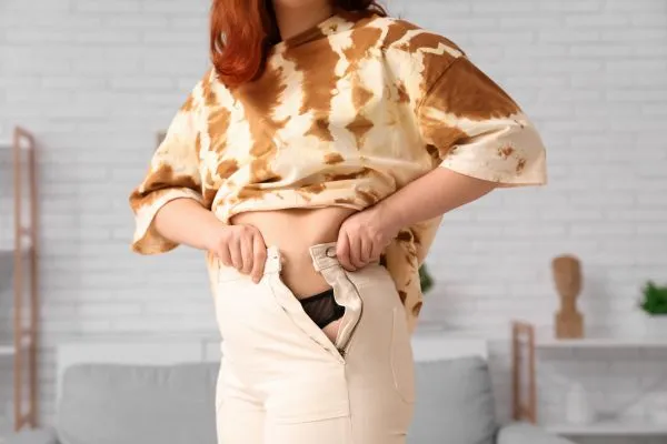 Image of woman trying to do her trousers up after pregnancy weight gain Bristol