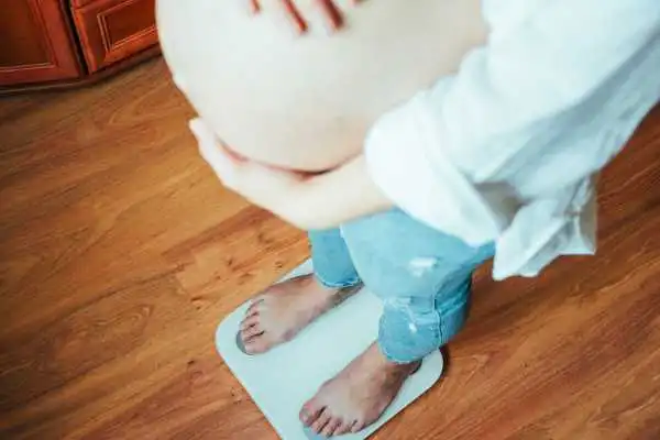 Image of woman weighing herself and experiencing weight gain through pregnancy Bristol